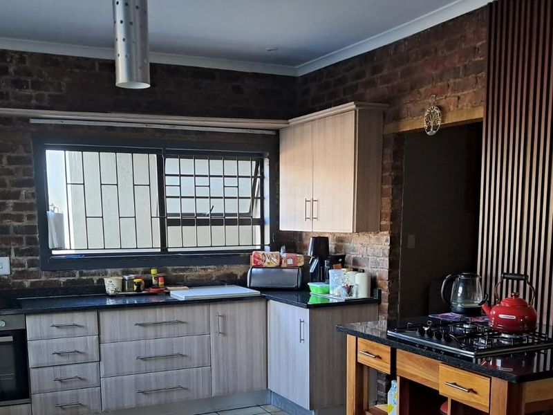 A modern kitchen featuring exposed brick walls, a timber slat feature wall, granite countertops, and built-in appliances including an oven and gas hob.