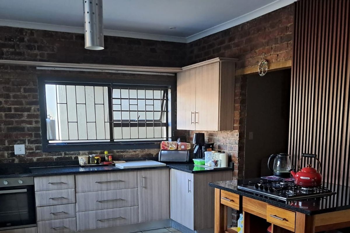 A modern kitchen featuring exposed brick walls, a timber slat feature wall, granite countertops, and built-in appliances including an oven and gas hob.