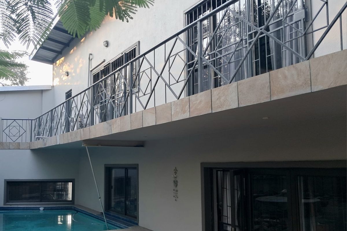 Rear exterior view of the house featuring a swimming pool, a balcony with decorative metal railings, and sliding door access to the interior.