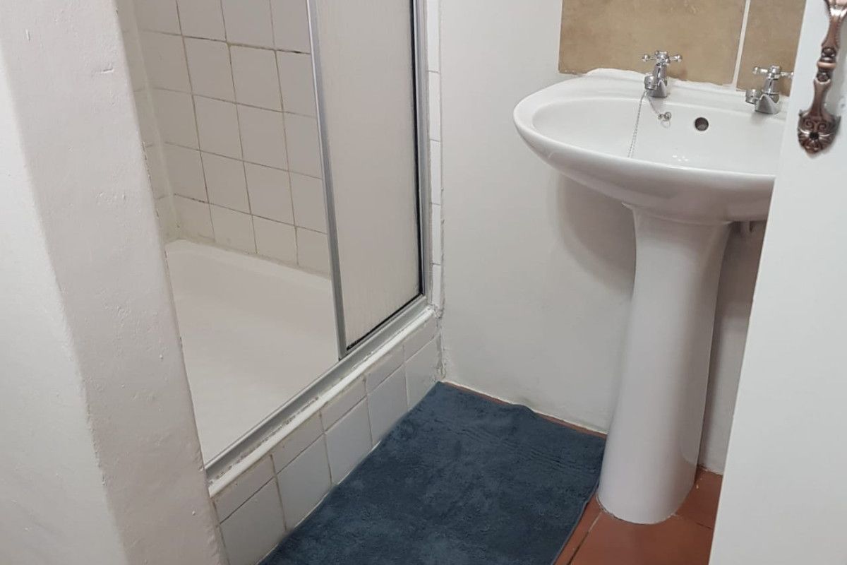 A compact bathroom featuring a pedestal basin and a shower enclosure with tiled finishes, requiring some cosmetic updates to improve its overall condition.
