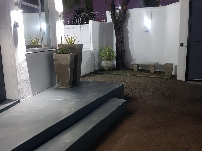 Night view of the property entrance featuring concrete steps, perimeter wall with security fencing, and exterior lighting.