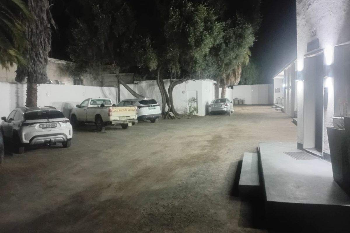 Night view of the rear exterior area featuring a large unpaved parking space, perimeter walls, and exterior building lighting.