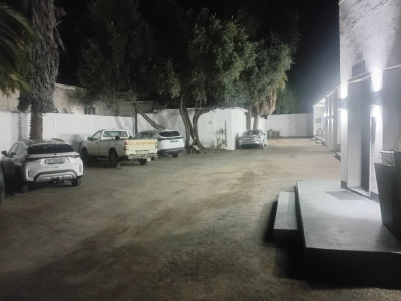 Night view of the rear exterior area featuring a large unpaved parking space, perimeter walls, and exterior building lighting.