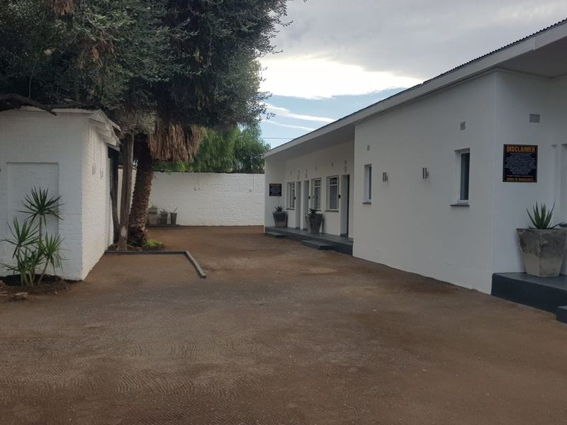 A view of the rear exterior area of the guest house, featuring white painted brick buildings and an unpaved ground surface.