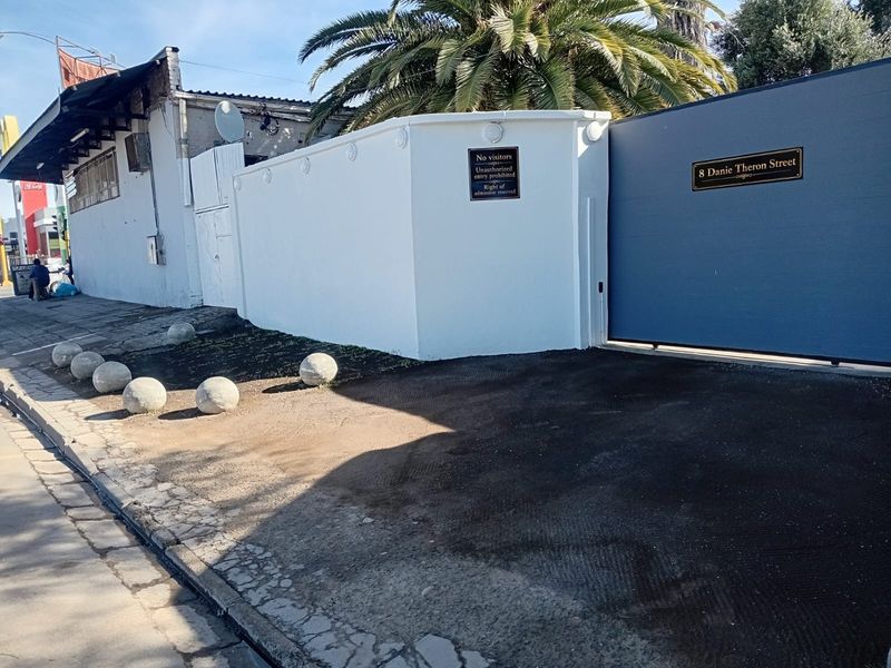Front exterior view of the property featuring a secure sliding gate, boundary wall, and paved driveway area with concrete bollards.