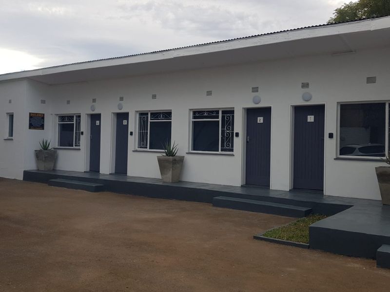 Exterior view of a guest house featuring multiple individual unit entrances with security doors and external lighting along a paved walkway.