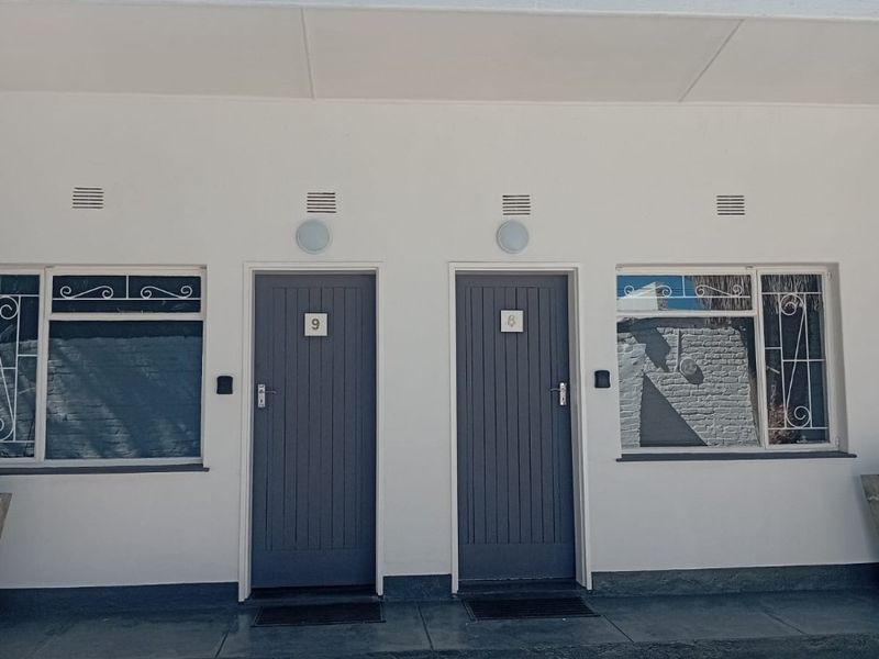 Front elevation of a guest house featuring two separate unit entrances with grey painted doors, security bars on windows, and exterior lighting.
