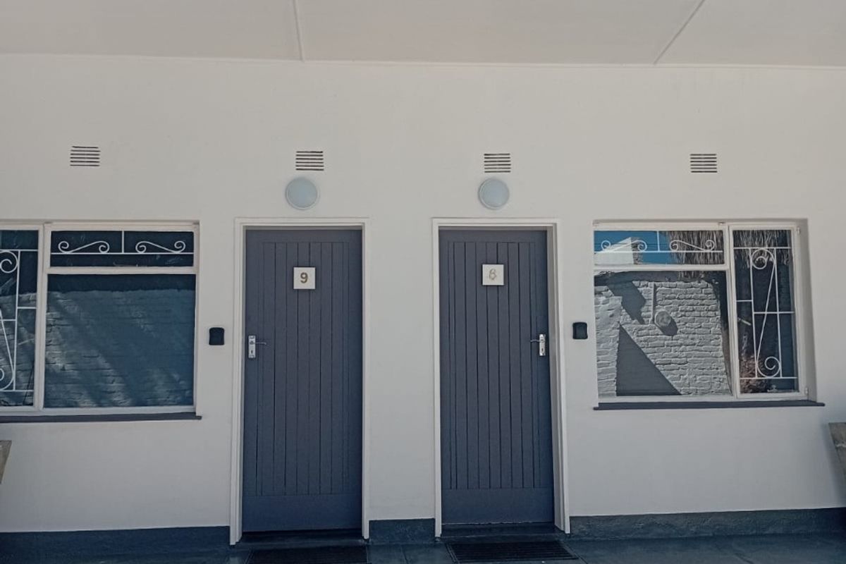Front elevation of a guest house featuring two separate unit entrances with grey painted doors, security bars on windows, and exterior lighting.