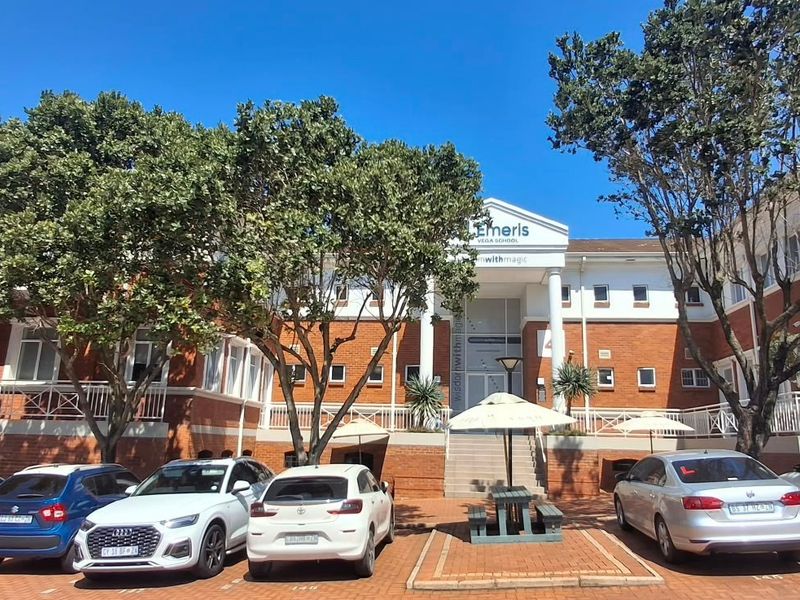 Front exterior view of a multi-story brick office building featuring a prominent entrance with columns and a paved parking area.