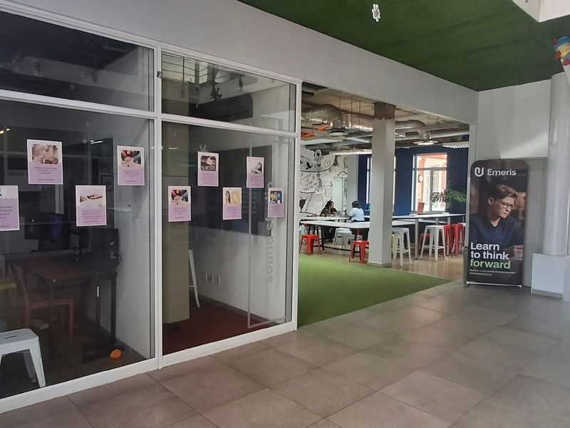 Modern open-plan office space featuring glass-partitioned meeting rooms, tiled flooring, and exposed industrial-style ceiling ducting with integrated lighting.