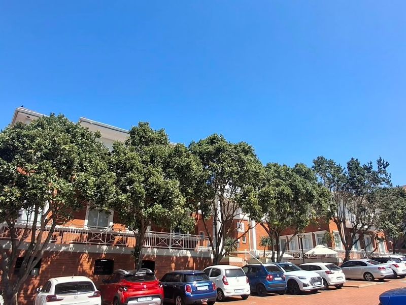 Rear view of a multi-story office building featuring a brick facade, balcony railings, and an adjacent paved parking area with mature trees.