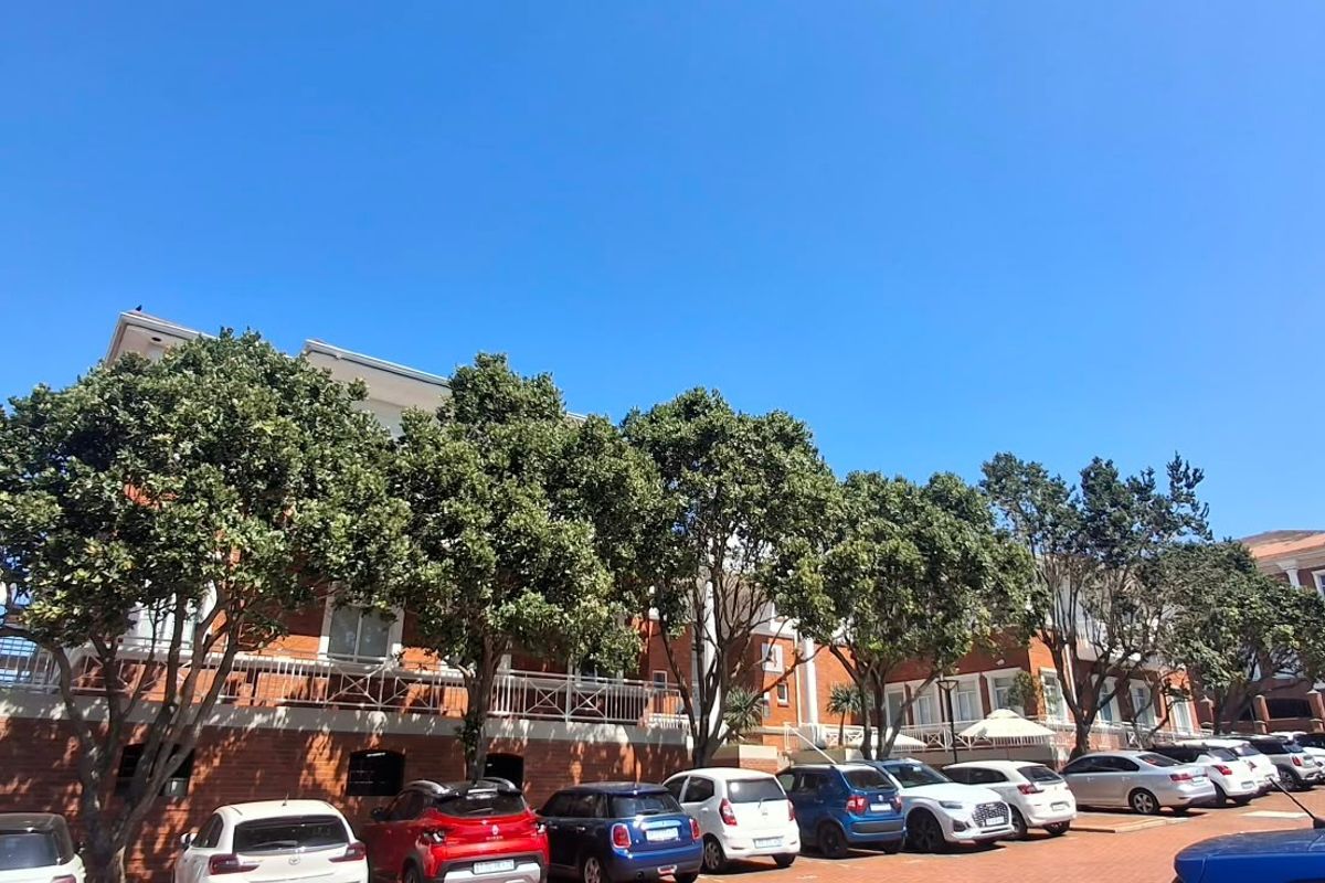 Rear view of a multi-story office building featuring a brick facade, balcony railings, and an adjacent paved parking area with mature trees.