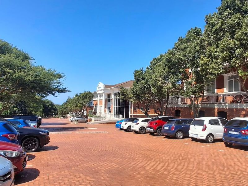 Exterior view of a multi-story office building featuring a large brick-paved parking area and mature landscaping.