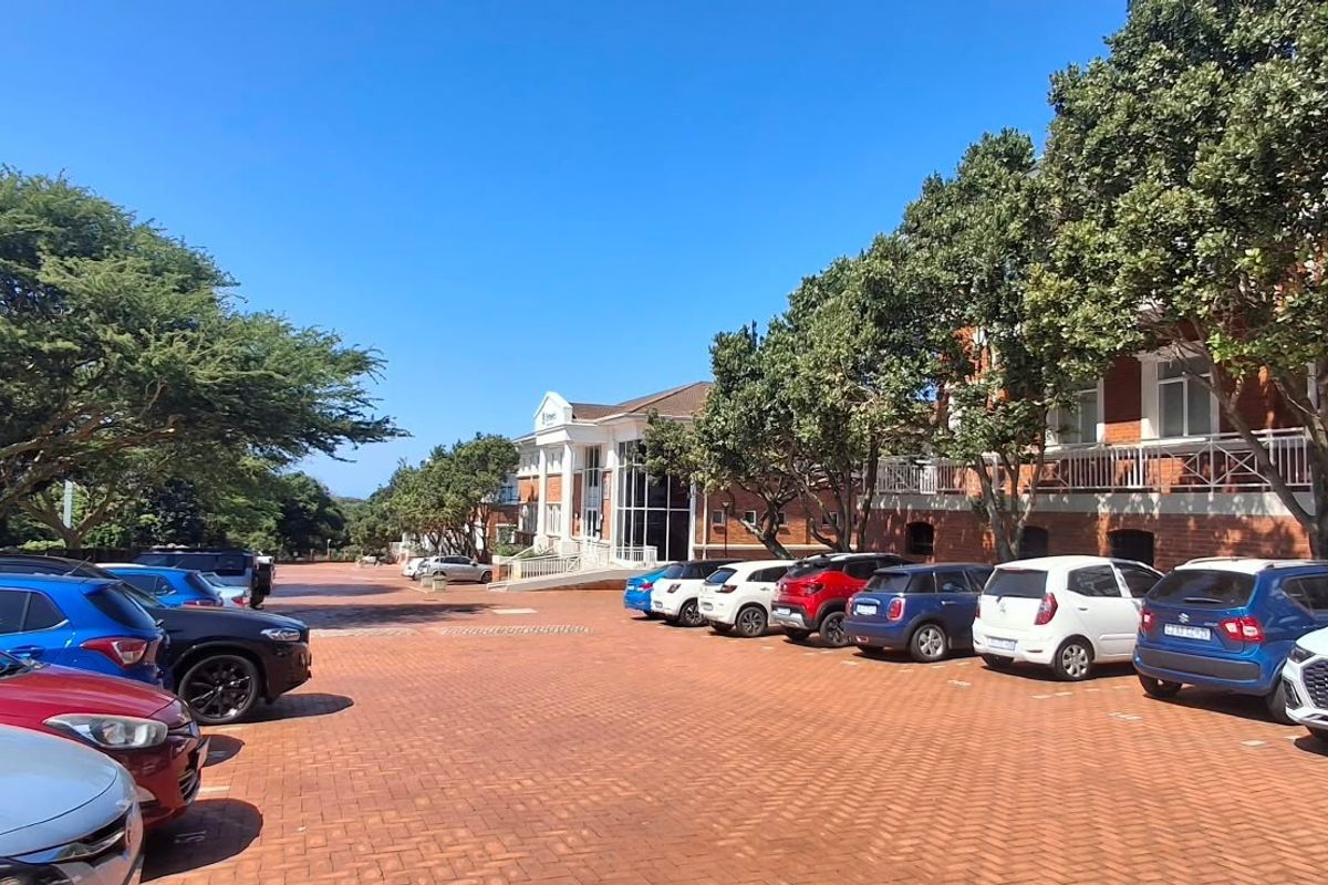 Exterior view of a multi-story office building featuring a large brick-paved parking area and mature landscaping.