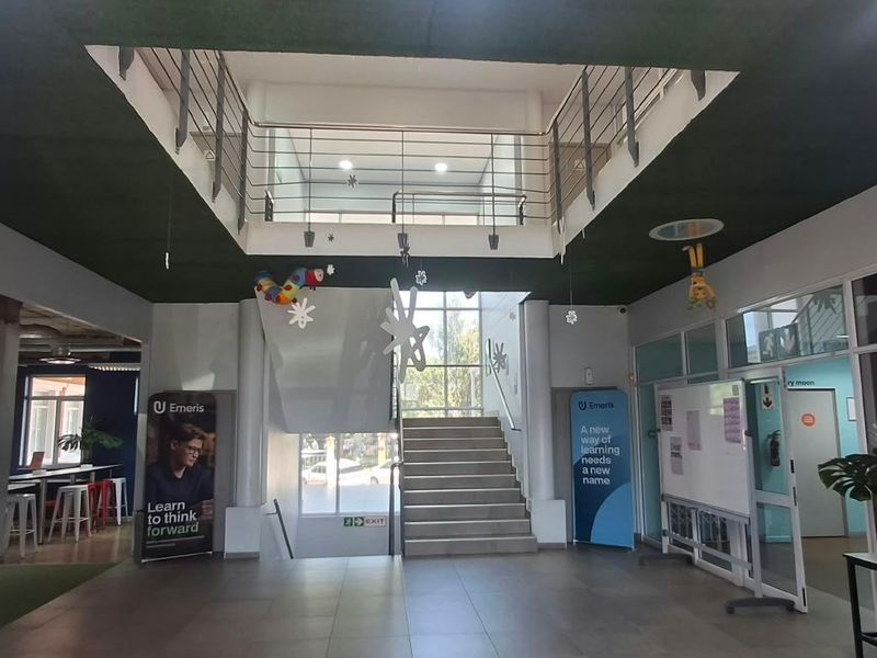 Spacious office building entrance foyer featuring a central staircase with metal balustrades, glass partitions, and modern tiled flooring.