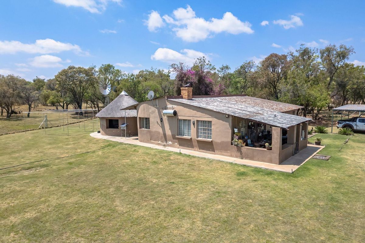 Aerial view of a farm property featuring a main dwelling with a combination of thatched and metal roofing, a windmill, and a covered patio area.