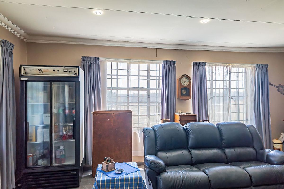 A living room featuring recessed downlighting, decorative cornicing, and large windows fitted with security bars, offering a functional space with potential for modernization.