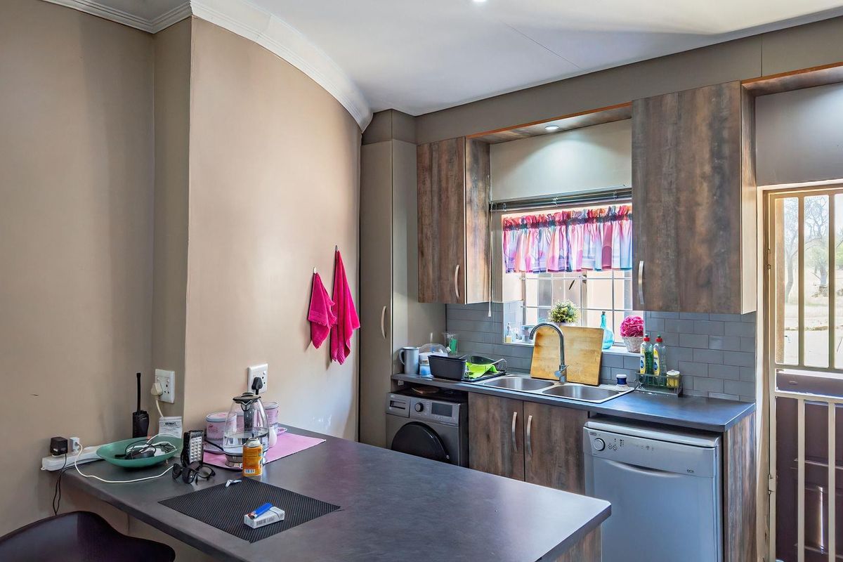 A functional kitchen featuring wood-look cabinetry, dark laminate countertops, a double sink, and integrated laundry appliances with direct access to the exterior.