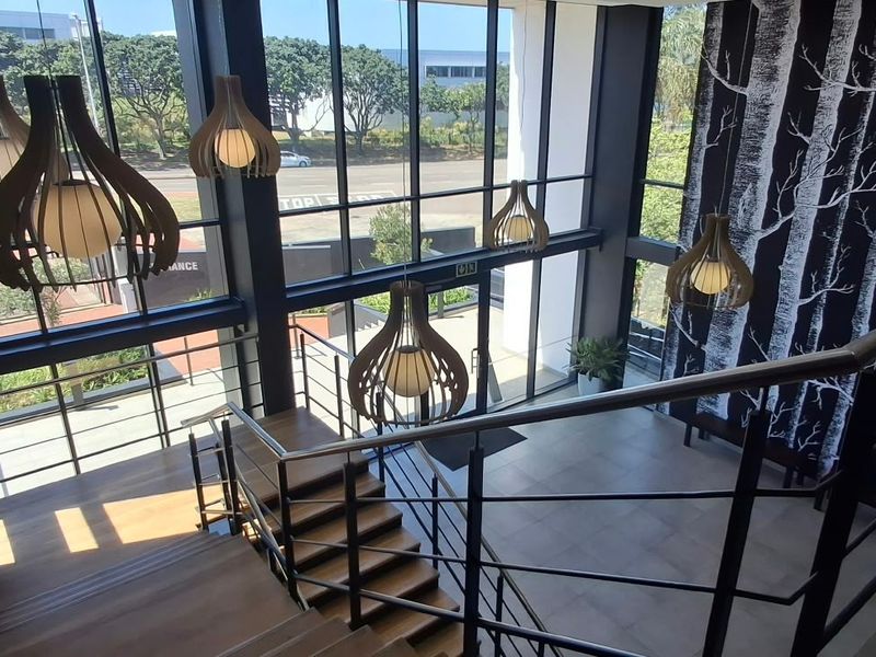 Modern commercial entrance lobby featuring a grand timber staircase, floor-to-ceiling glass windows, and contemporary pendant lighting in a bright, open-plan space.