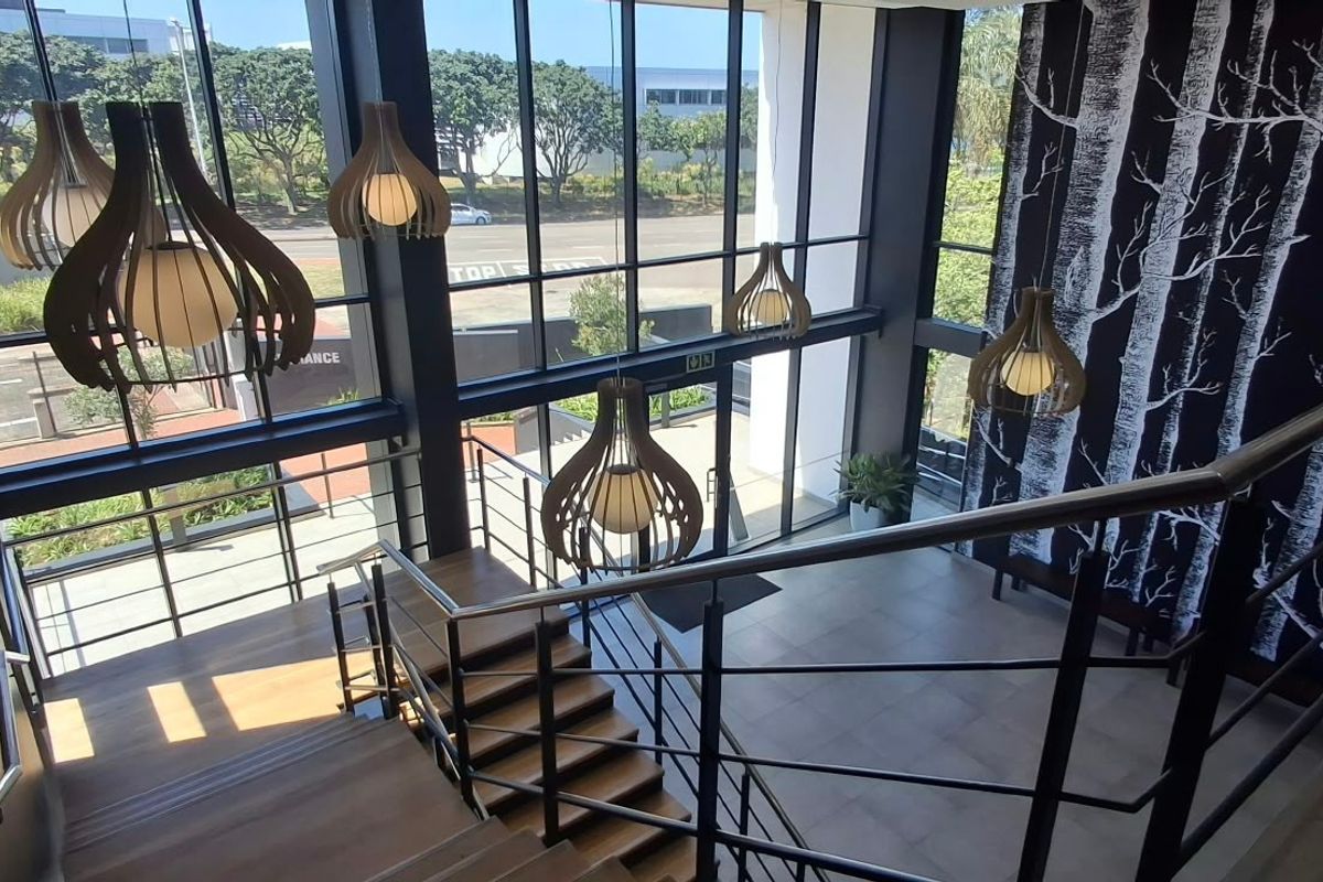 Modern commercial entrance lobby featuring a grand timber staircase, floor-to-ceiling glass windows, and contemporary pendant lighting in a bright, open-plan space.