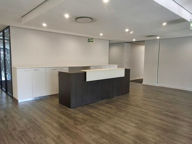 Modern commercial reception area featuring a built-in desk, sleek cabinetry, recessed lighting, and glass partitions, offering a professional and clean entrance space.