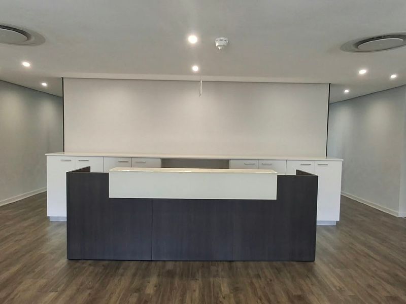 A modern, professional reception area featuring a built-in desk, clean cabinetry, recessed lighting, and high-quality laminate flooring in a neutral, well-maintained office space.