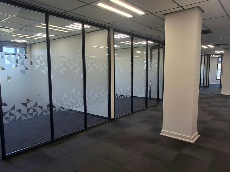 Modern open-plan commercial office space featuring glass partitioned offices, suspended ceilings, recessed lighting, and carpeted flooring.