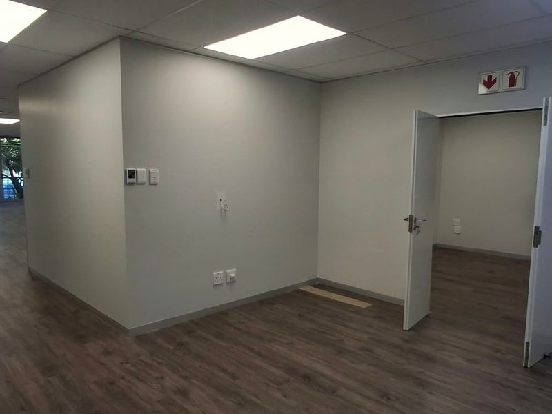 Spacious open-plan office area featuring modern laminate flooring, recessed ceiling lights, and a separate partitioned room with double door access.