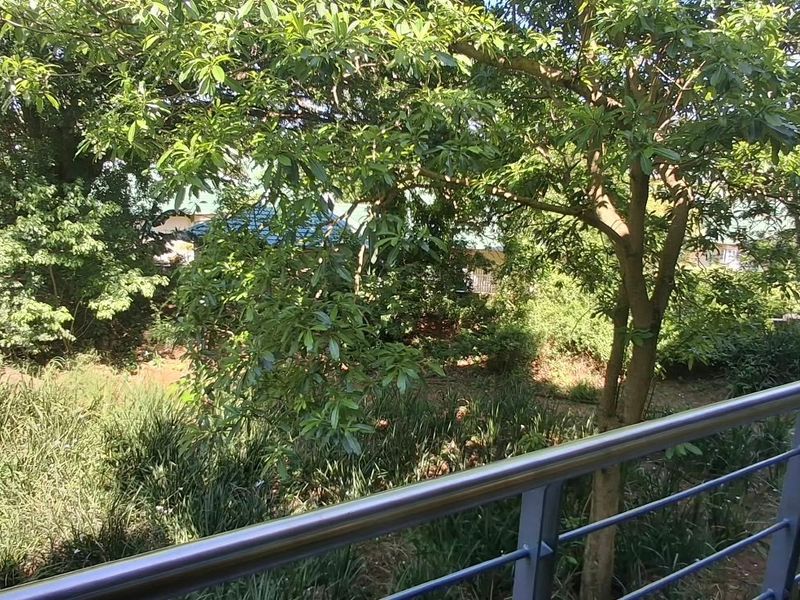 A balcony featuring a modern metal balustrade overlooking a lush, tree-filled garden area.