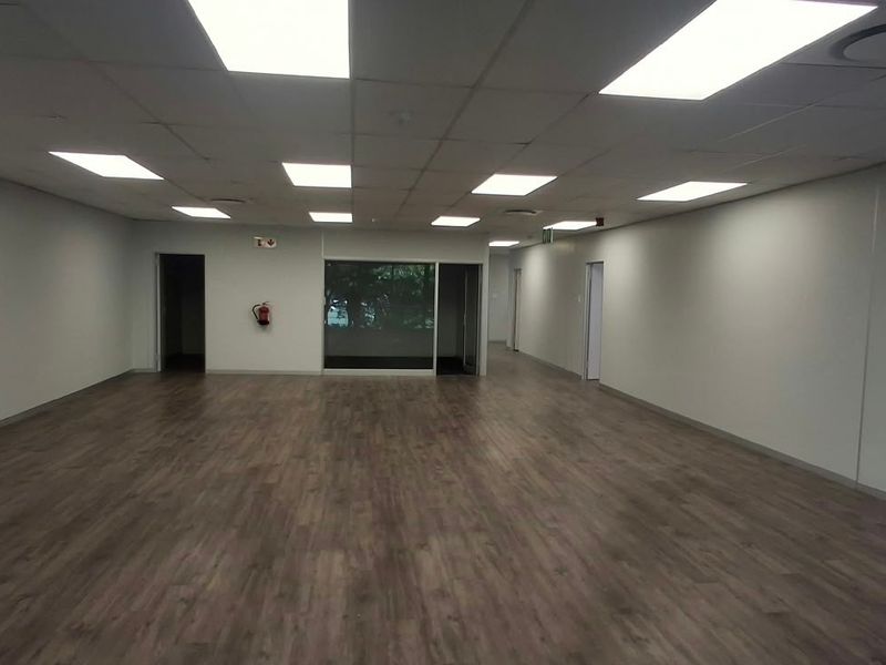 A spacious, open-plan office area featuring modern laminate flooring, a suspended ceiling with recessed lighting, and a glass partition.