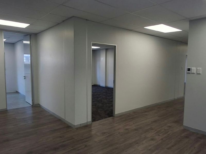 A clean, vacant office space featuring modern laminate flooring, recessed lighting, and neutral wall finishes, providing a versatile environment for professional use.