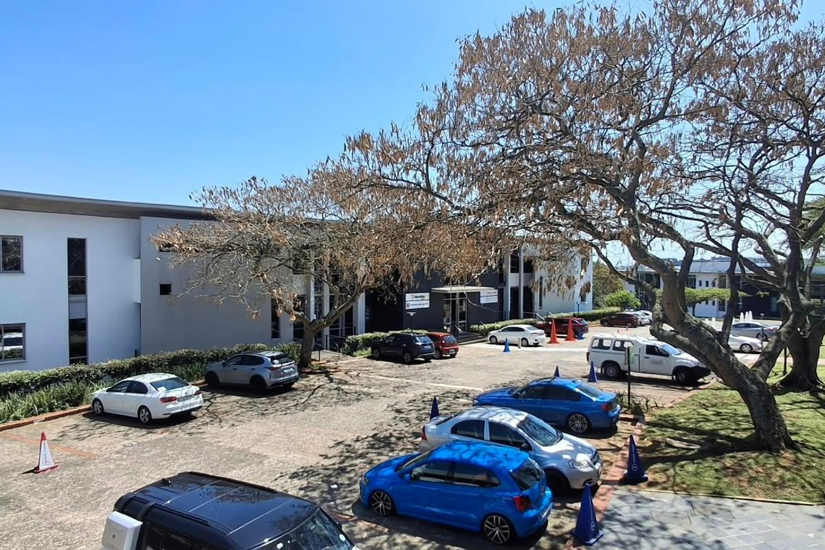 An elevated view of the office building exterior, featuring a paved parking area, landscaped grounds, and mature trees surrounding the professional premises.
