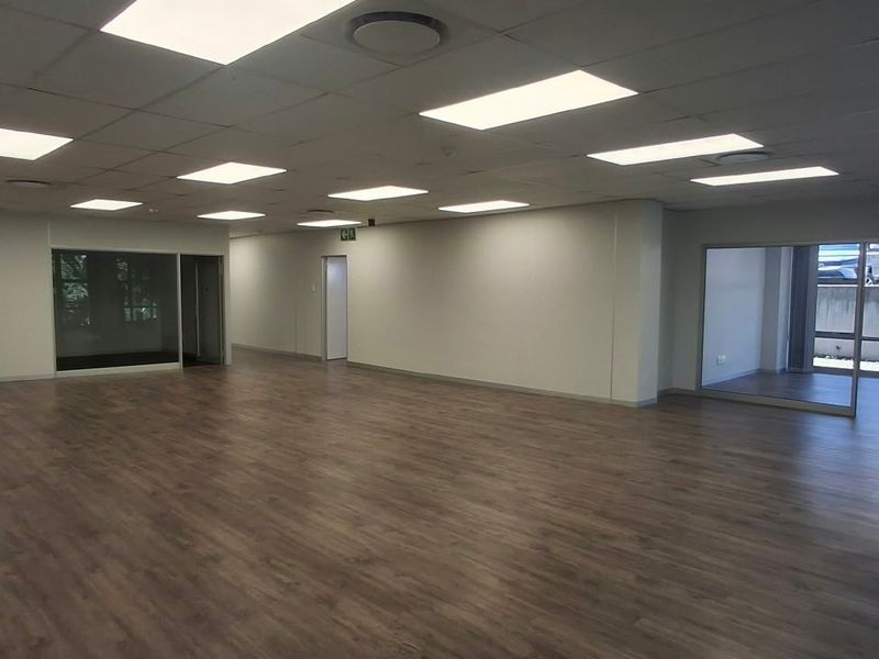 Spacious, open-plan office area featuring modern laminate wood flooring, recessed LED panel lighting, and glass partition walls, offering a bright and professional workspace.