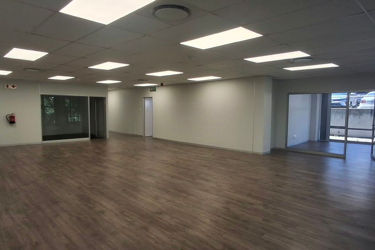 Spacious, open-plan office area featuring modern laminate wood flooring, recessed LED panel lighting, and glass partition walls, offering a bright and professional workspace.