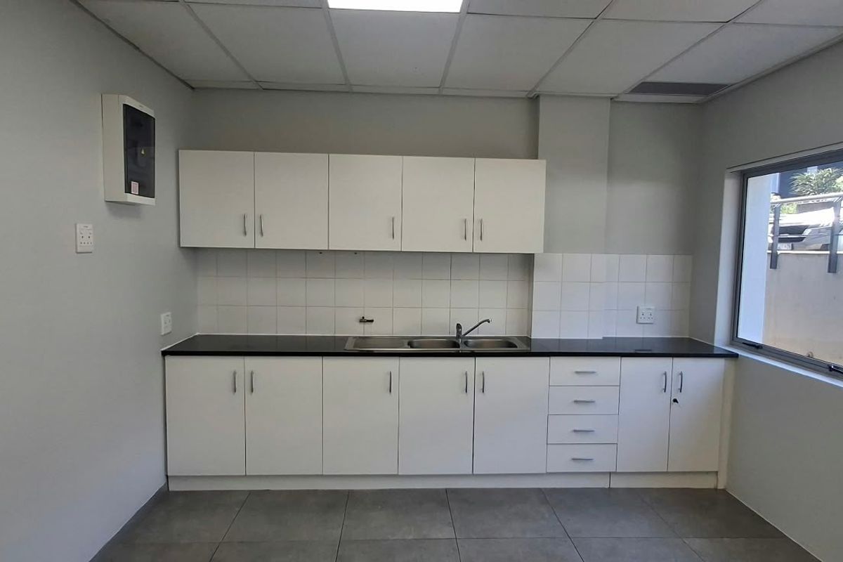 A clean and functional office kitchenette featuring white cabinetry, a dark countertop, stainless steel sink, and tiled flooring.