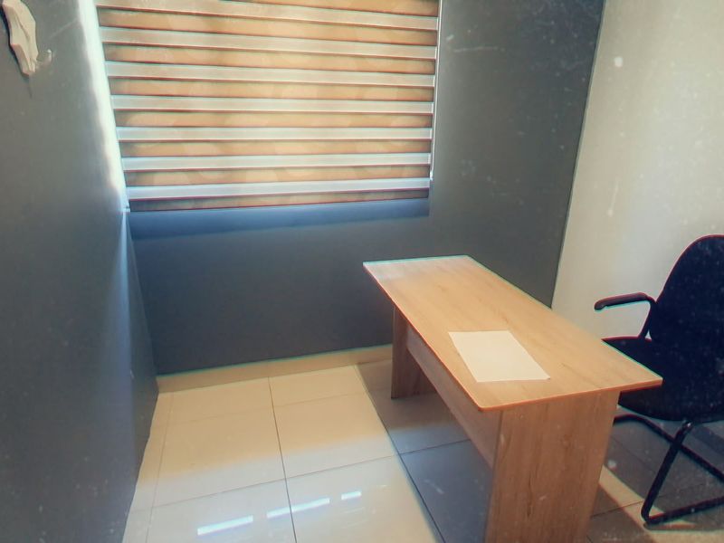 A compact office space featuring tiled flooring and modern venetian blinds, providing a functional environment for professional use.