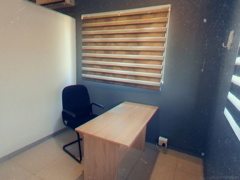 A compact office space featuring tiled flooring, modern roller blinds, and an integrated air conditioning unit, providing a functional workspace environment.