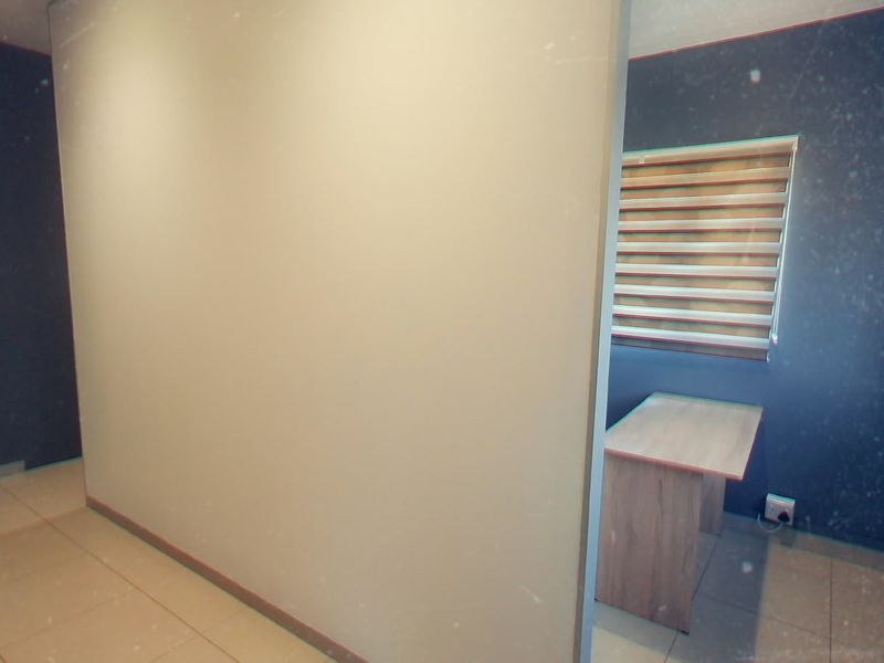 A compact office space featuring tiled flooring, a built-in desk, and modern roller blinds, providing a functional workspace environment.