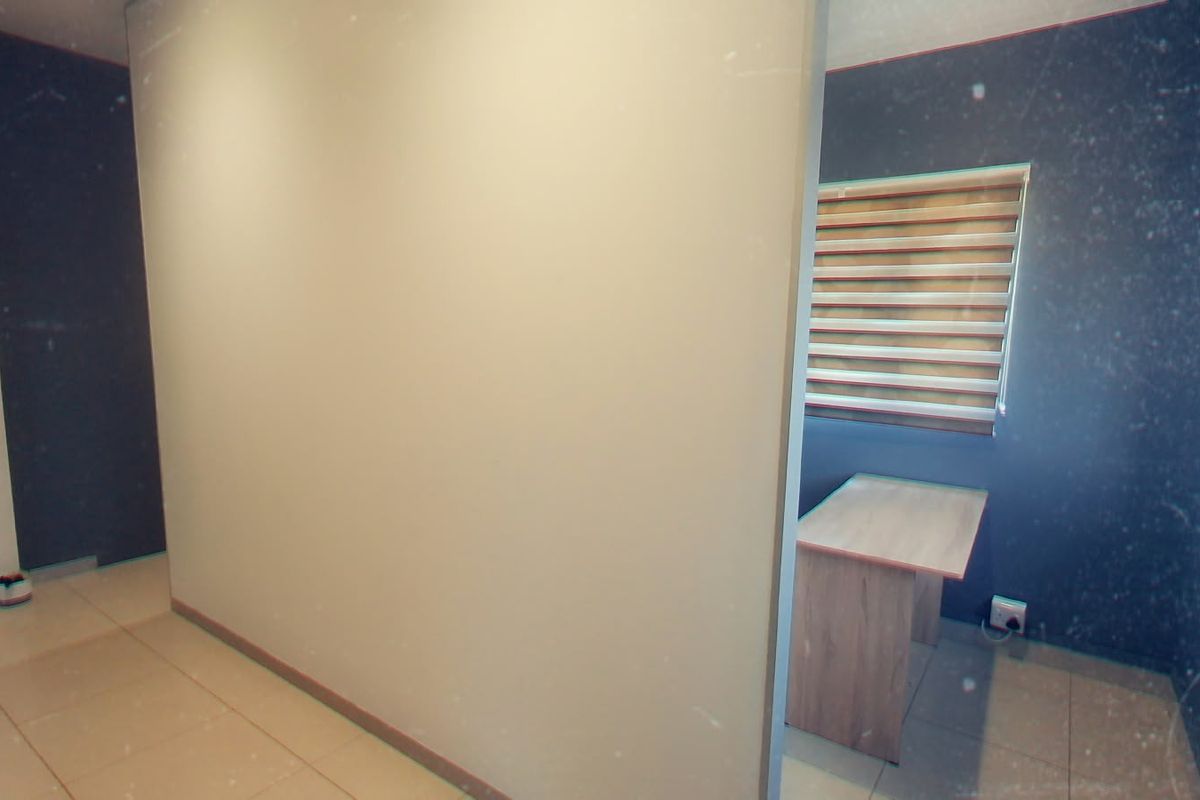 A compact office space featuring tiled flooring, a built-in desk, and modern roller blinds, providing a functional workspace environment.