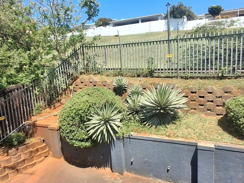 Rear outdoor area featuring tiered retaining walls, steel palisade fencing with electric security, and paved ground space.