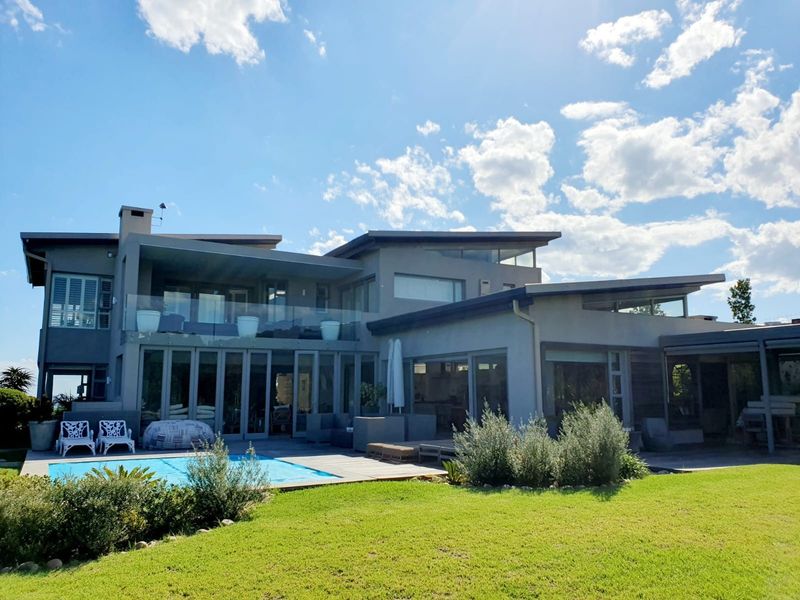 Rear view of a modern multi-level residence featuring a swimming pool, expansive glass sliding doors, and a covered patio area overlooking the garden.