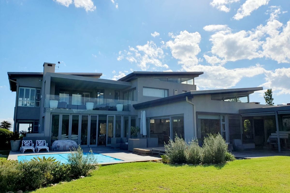 Rear view of a modern multi-level residence featuring a swimming pool, expansive glass sliding doors, and a covered patio area overlooking the garden.