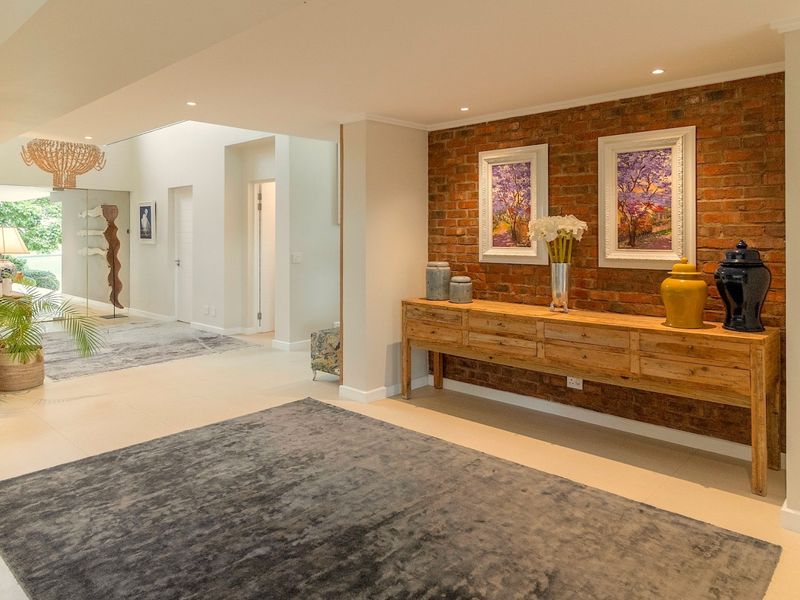 Spacious living area featuring a striking exposed brick feature wall, neutral tiled flooring, and modern recessed downlighting throughout the open-plan space.