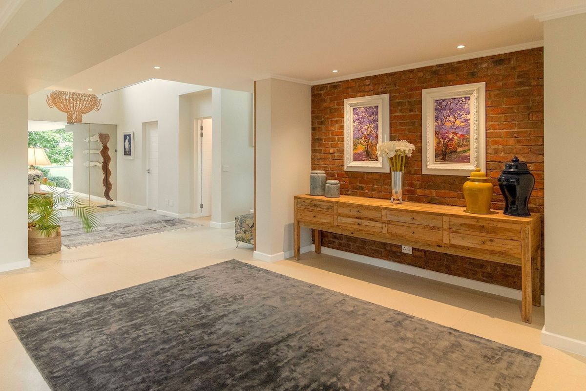 Spacious living area featuring a striking exposed brick feature wall, neutral tiled flooring, and modern recessed downlighting throughout the open-plan space.