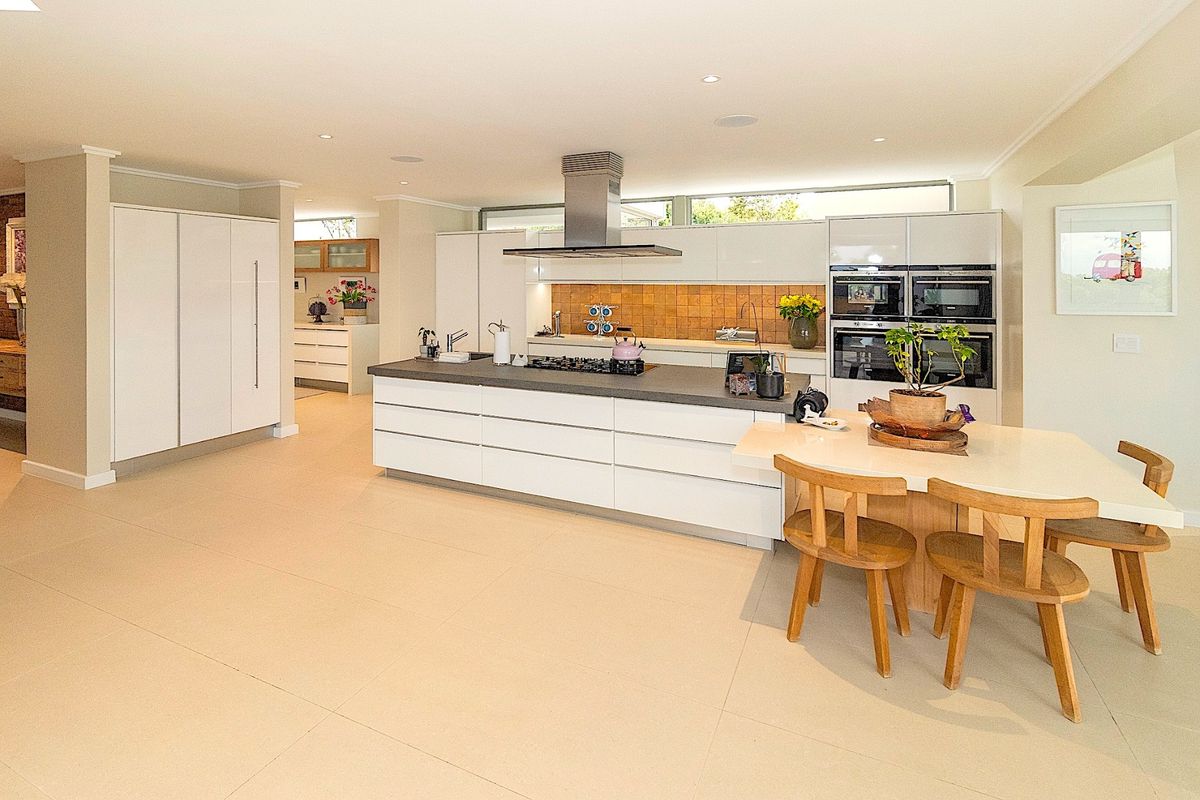 Modern, spacious kitchen featuring a large central island, high-end built-in appliances, sleek white cabinetry, and a stylish tiled splashback in an open-plan layout.