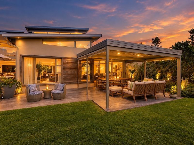 A beautifully landscaped rear garden featuring a modern covered patio with timber decking, integrated lighting, and seamless indoor-outdoor flow through large sliding glass doors.