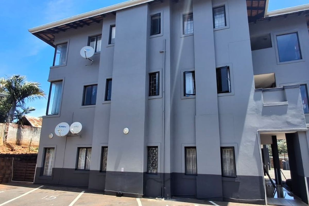 A multi-story residential building facade featuring grey exterior paint, designated parking bays, and secure window treatments.