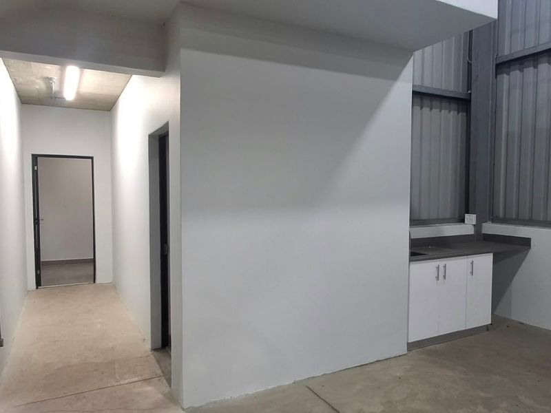A clean industrial utility space featuring built-in cabinetry with a sink, fire safety equipment, and high-ceiling corrugated metal wall cladding.