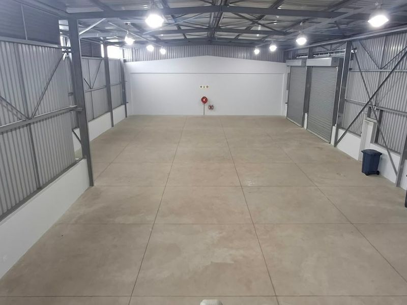Spacious industrial warehouse unit featuring high ceilings, concrete flooring, roller shutter access, and integrated fire safety equipment.