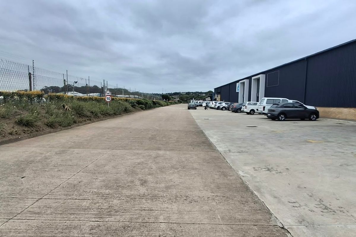 Industrial property exterior featuring a large concrete driveway, metal cladding facade, and secure perimeter electric fencing.